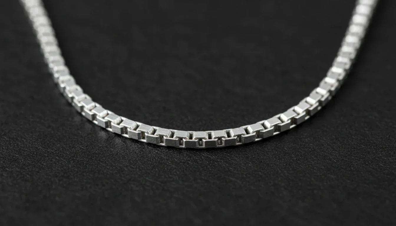 Photo - Close-up of a silver necklace showing what is a box chain structure on a dark surface.webp