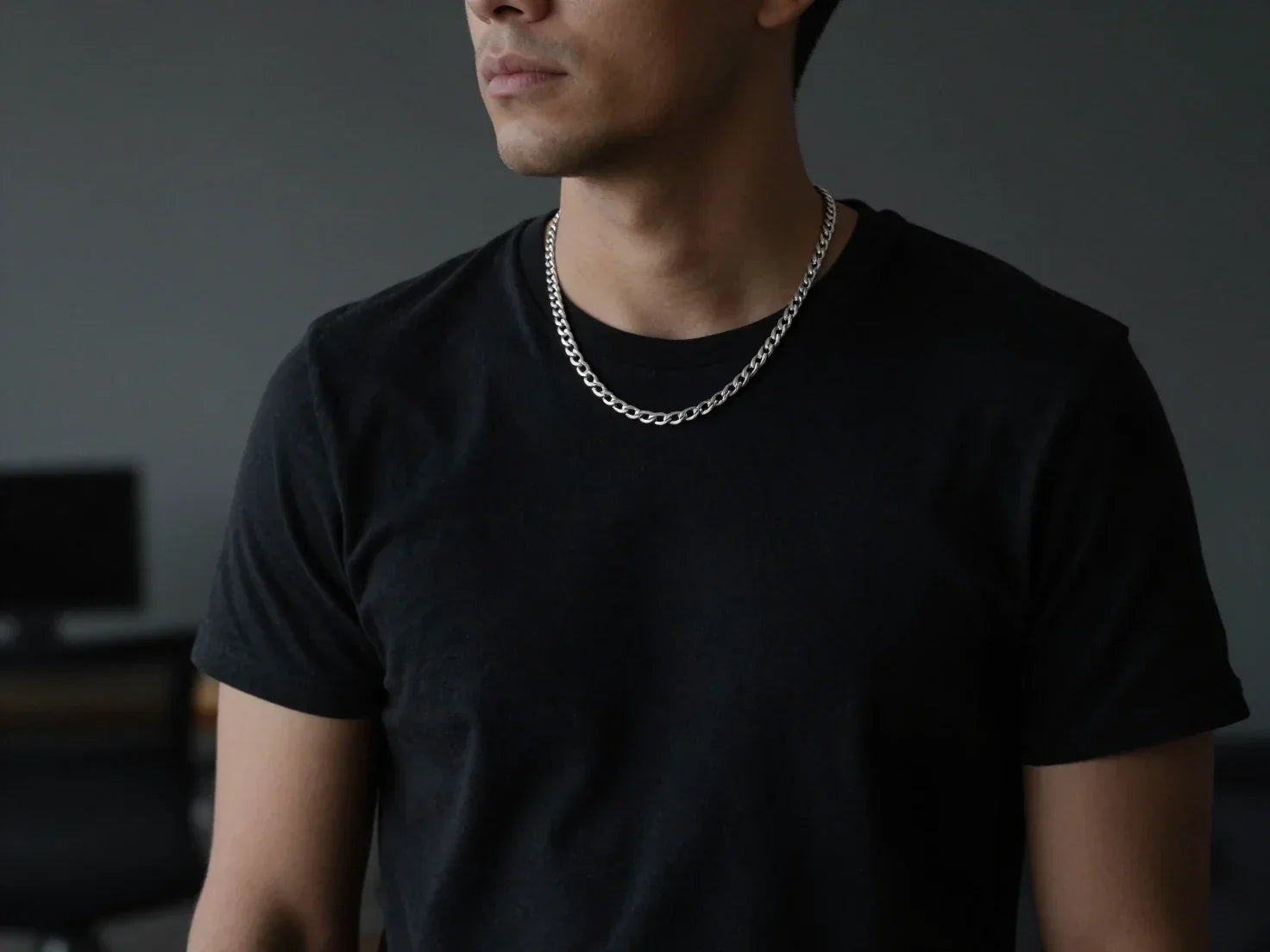 Photo – Man in a black fitted t-shirt in a modern office setting, wearing a solid sterling silver Cuban chain that represents a strongest chain type built for everyday routine and clean structure